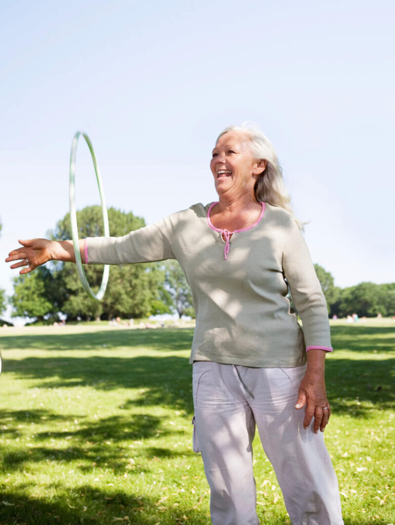 Sportowy look starszej kobiety: jasna koszulka z długim rękawem i białe lniane spodnie