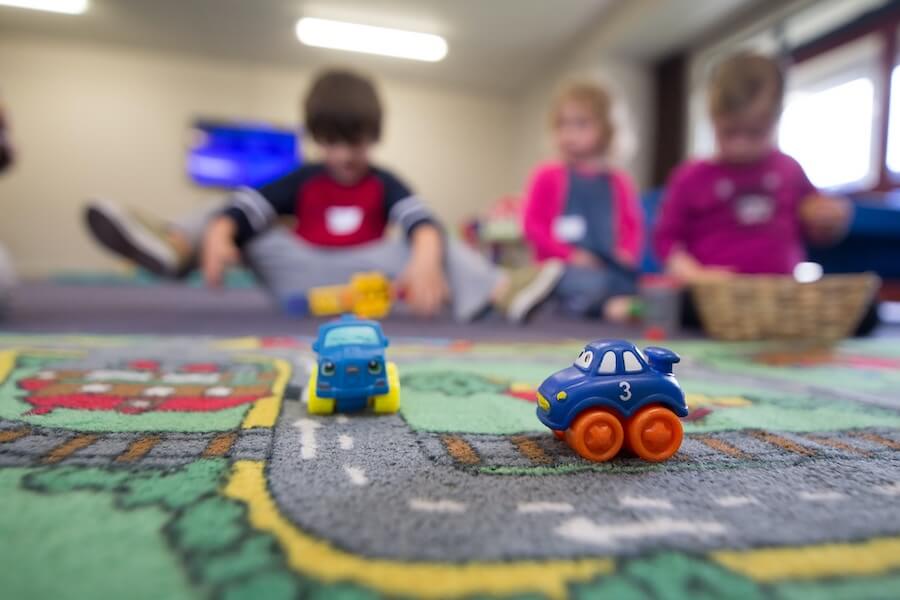 zabawki na dywanie w przedszkolu, w tle trójka bawiących się dzieci