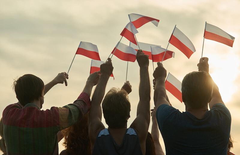 młodzi ludzie unoszący w górę polskie flagi