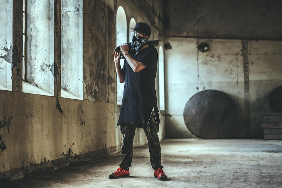 Mężczyzna w ubraniach oversize z bandamą zakrywajacą twarz i deskorolką