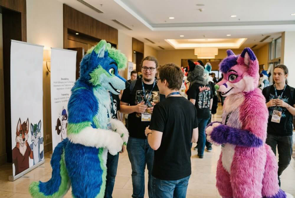 Uczestnicy konwentu furry w hotelowym lobby, część w fursuitach, część bez strojów, w atmosferze spotkania społeczności