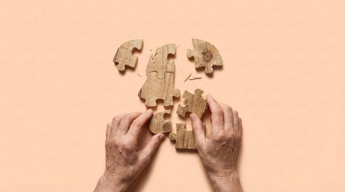 Dłonie układające rozrzucone drewniane puzzle w kształcie twarzy